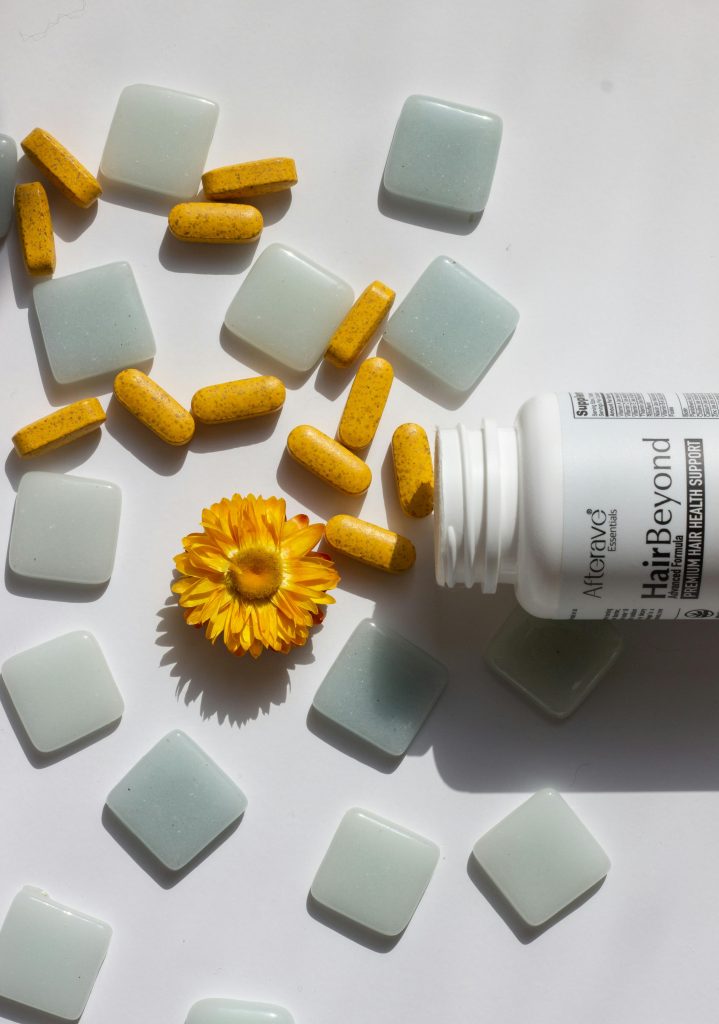 Hair vitamins beside a marigold flower on a white background.