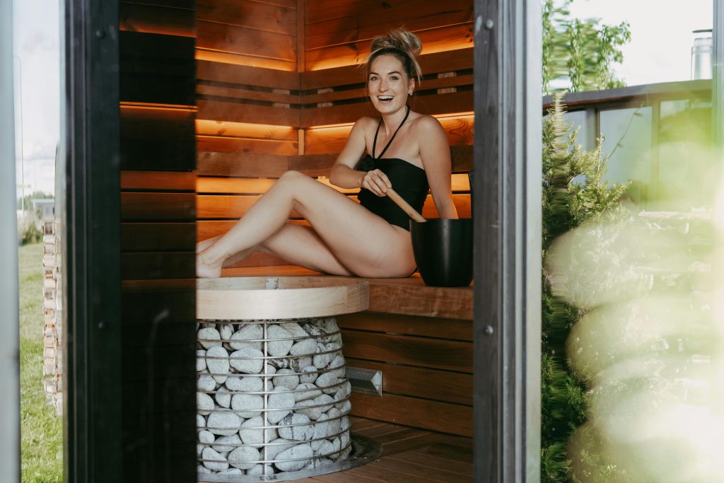A woman enjoying a relaxing moment inside a modern sauna, showcasing wooden design and sauna stones.