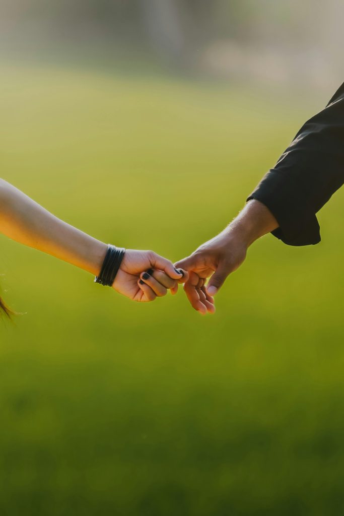 A couple holding hands in a green outdoor setting, symbolizing love and connection.