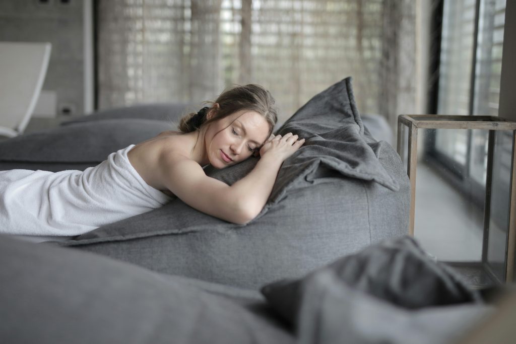 Woman peacefully relaxing at a spa, wrapped in a towel on a comfortable bed, enjoying serene ambiance.
