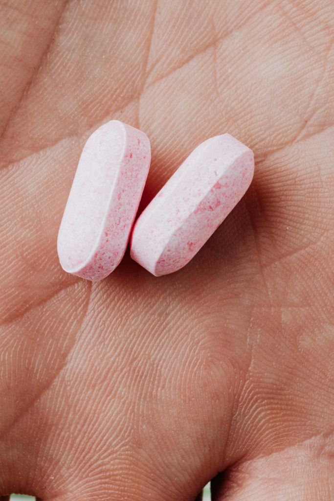 Detailed close-up of two pink pills resting in an adult hand, representing medication or supplements.