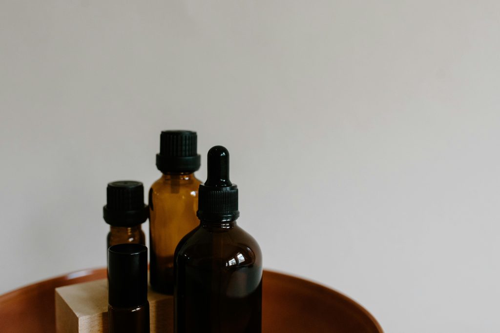 A minimalist arrangement of amber essential oil bottles with dropper and spray tops on a wooden tray.