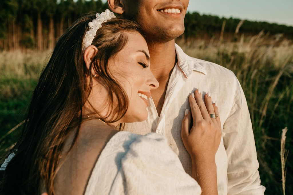 A young couple embraces in a sunlit meadow, enjoying a romantic and happy moment together.