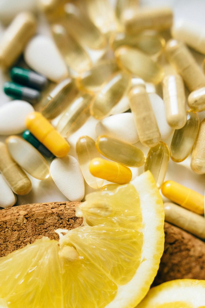 Close-up of assorted vitamins, supplements, and lemon slices on a cork surface.