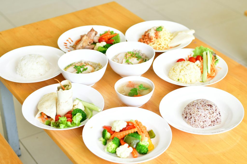 A variety of healthy dishes including rice, soup, and vegetables served on a wooden table.