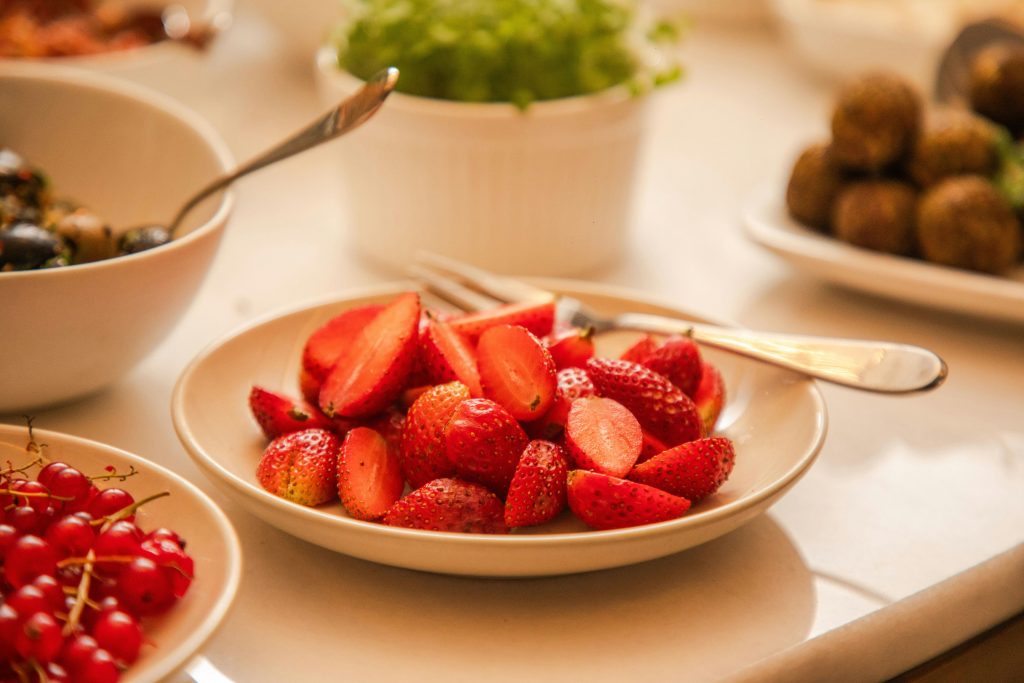 Close-up of fresh strawberries in a bowl with spoons, surrounded by various dishes.