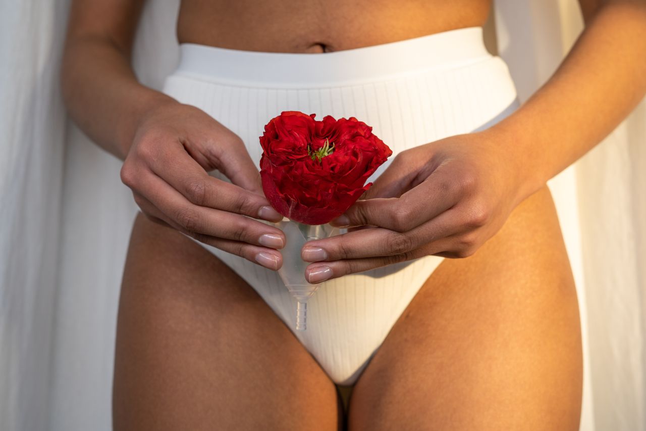 Close-up of woman holding a reusable menstrual cup with a red rose, promoting eco-friendly feminine hygiene.